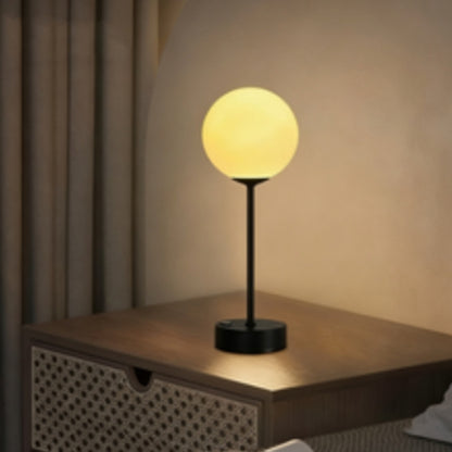 Aurum luminária de mesa dourada com globo acrílico acesa sobre criado-mudo